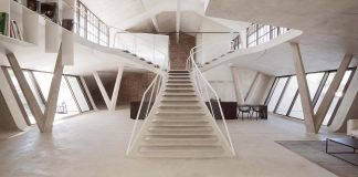 Rounded concrete staircase opens up all rooms and also appears to be carrying them